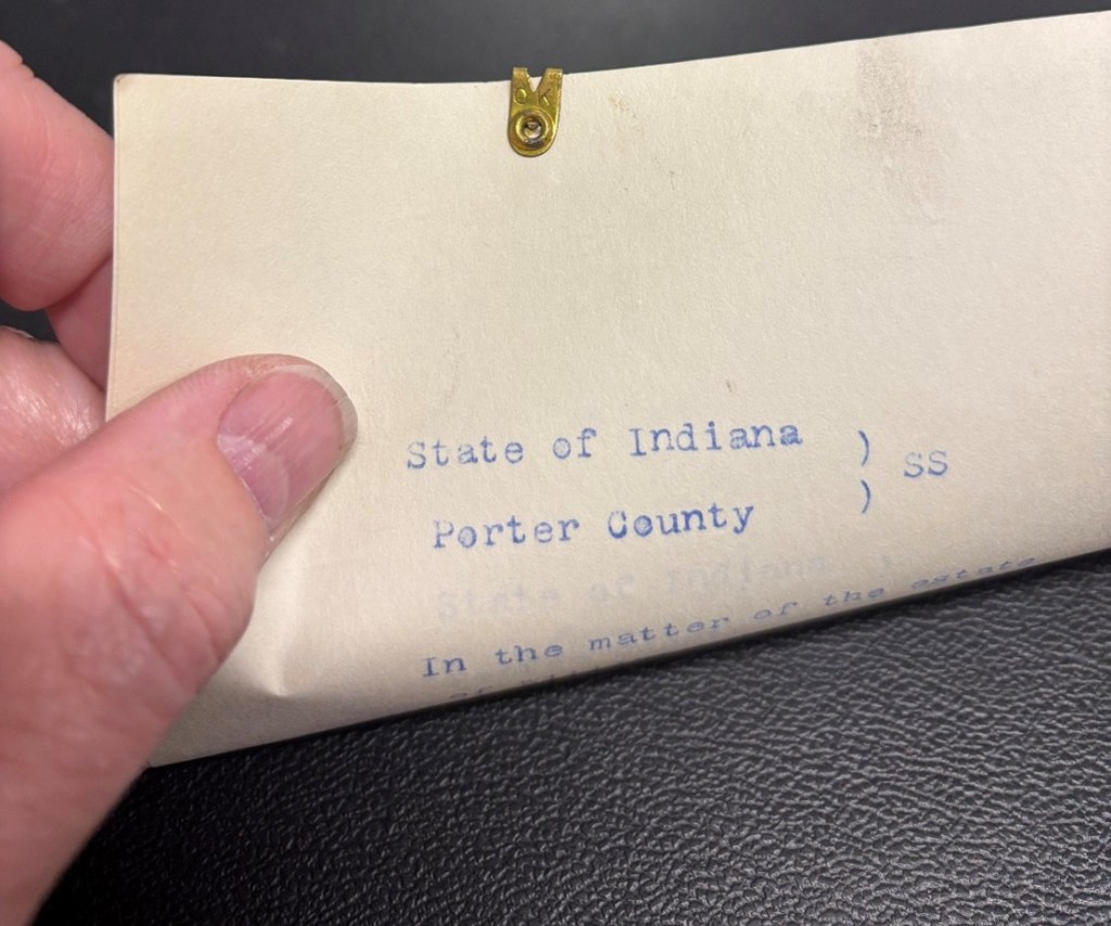 A close-up view of a document labeled 'State of Indiana, Porter County' held by a hand, featuring printed text and a small brass clasp.