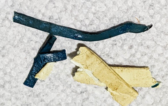 Three pieces of material including two sections in dark blue and one in yellowish color, placed on a textured white surface.